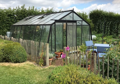 Serres en verre trempée dans un jardin avec palissade en bois 