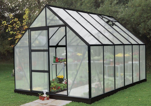 Serre en polycarbonate avec porte coulissante et lucarne dans un jardin où poussent des plantes et des fleurs