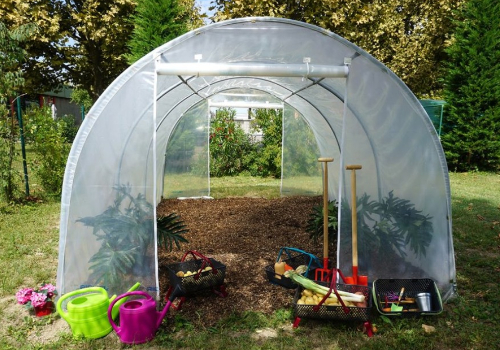 serre tunnel dans un jardin avec de terre retournée et outils de jardinage